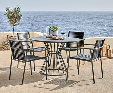 Kerek szürke kerti asztal és fekete kerti székek egy teraszon a tengerparton