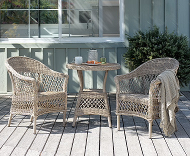 Világos színű kerek kávézó asztal két székkel egy teraszon a kertben