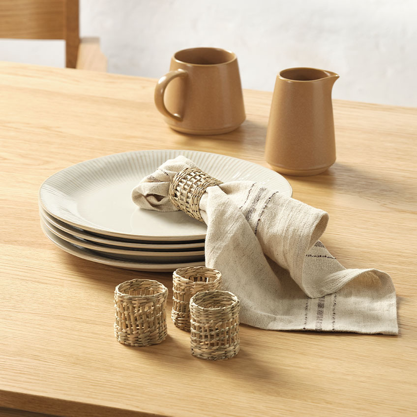 Fehér fordros szélű tányérok, tejkiöntő, textil szalvéta és szalvétagyűrűk egy étkezőasztalon