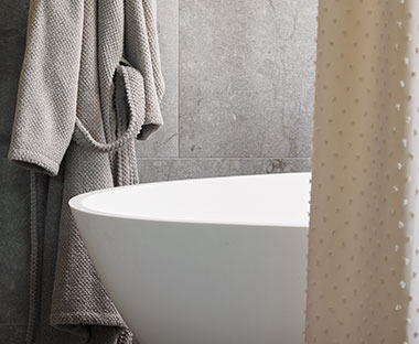 Bézs színű zuhanyfüggöny a háttérben káddal és fürdőköpennyel