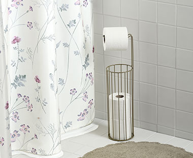 Virágmintás zuhanyfüggöny előtte WC-papír tartóval és kádkilépővel
