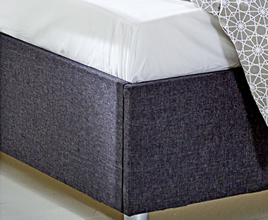 Egyszerű, kényelmes fehér lepedő szürke ágy sarkán 