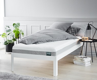 Habszivacs matrac ágyon szürke ágyneművel, éjjeliszekrény és szobanövény