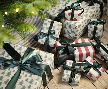 Karácsonyi mintájú csomagolópapírba csomagolt ajándékok egy karácsonyfa alatt