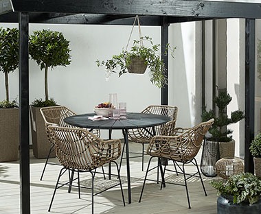 Stílusos fekete műfa asztal teraszon növényekkel és polyrattan székekkel