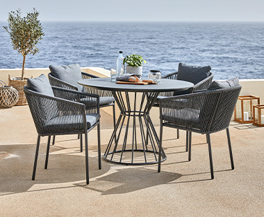Kerek szürke kerti asztal és szürke kerti székek egy teraszon a tengerparton