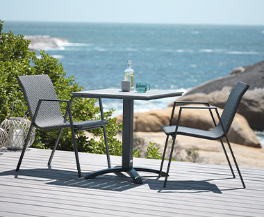 Fekete kerti asztal és szürke kerti székek egy teraszon a tengerparton