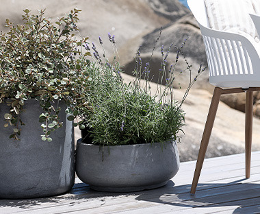 Szürke kaspók bennük növényekkel egy kerti szék mellett