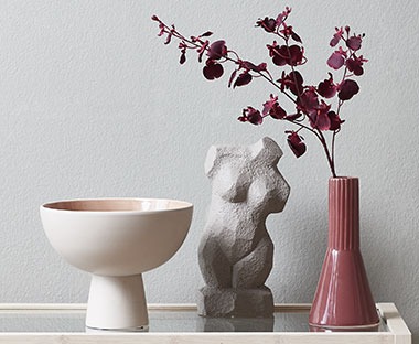 Szürke szobor mécsessel és vázával az asztalon