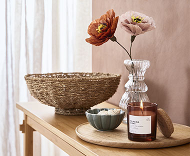 Átlátszó váza benne két művirággal, mellette illatgyertyával és tálkával egy asztalon 