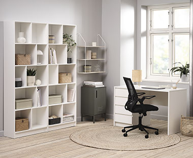 Fekete hálós irodaszék, fehér könyvespolc és íróasztal egy dolgozószobában