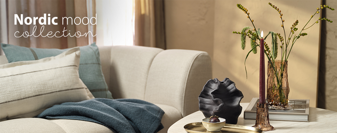 GUDMUND LED kúpos gyertya, VILHELM váza, OTTO üveg váza és gyertyatartó, VICTOR tál és KLOKKELYNG és HALLON díszpárnák Nappali kanapéval és egy dohányzóasztallal, üvegvázával és gyertyatartóval