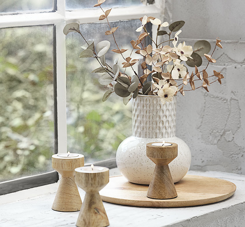 Világos bézs és fehér dombornyomott váza művirágokkal és fából készült mécsestartókkal