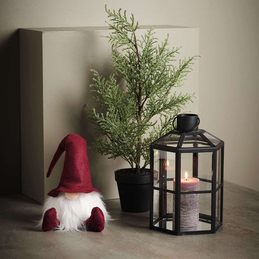 Skandináv karácsonyi manó egy műnövény és lámpás mellett