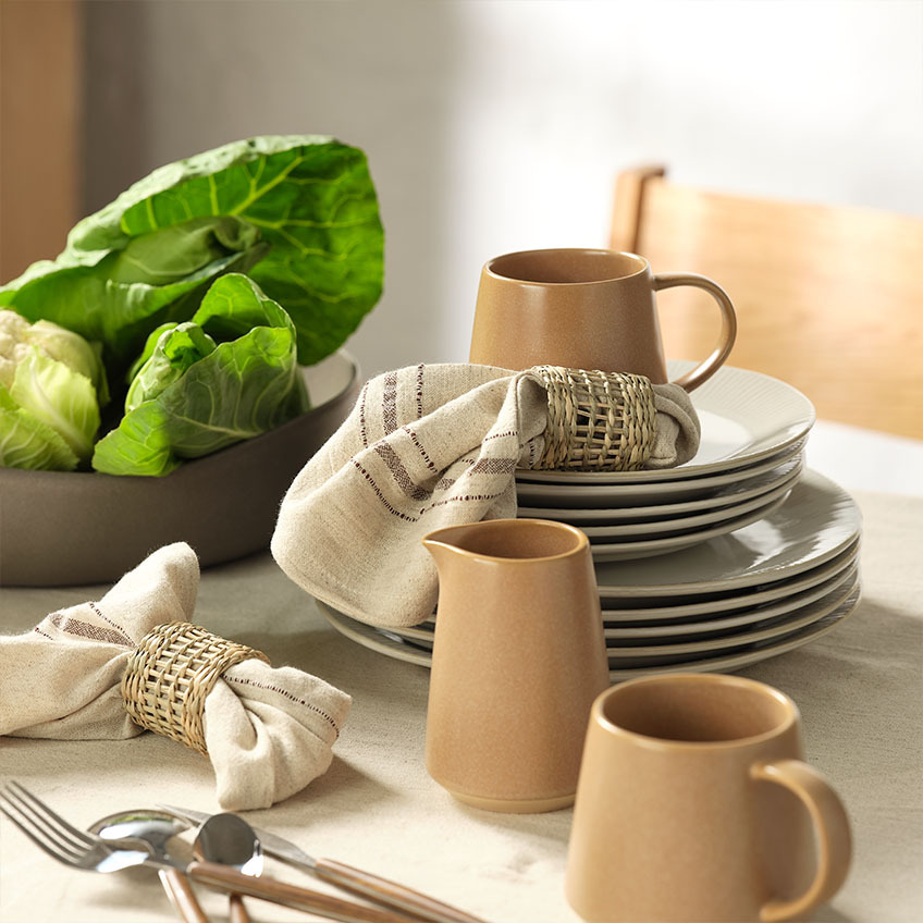 Étkészlet: Fehér tányérok és desszertes tányérok, bögre, tejkiöntő, textil szalvéták szalvétagyűrűvel és salátás tál egy étkezőasztalon
