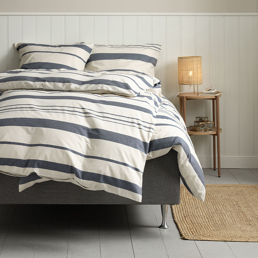 Pamut ágyneműhuzat fehér és kék csíkokkal az ágyra terítve egy hálószobában