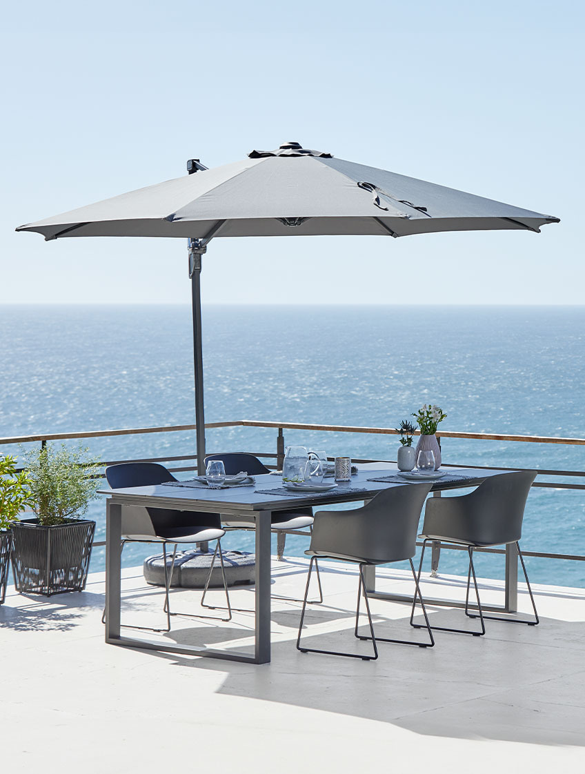 Nagyméretű függő napernyő kerti asztallal és székekkel egy teraszon az óceán mellett