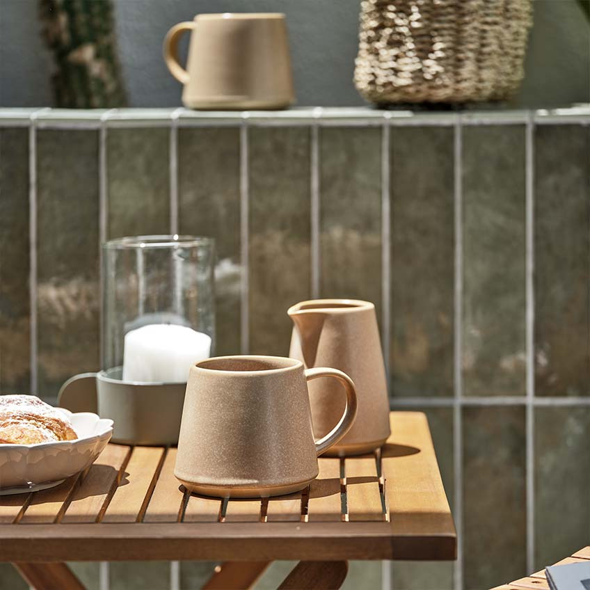 Kávésbögre és tejes kancsó egy kis kerti faasztalon a napsütésben