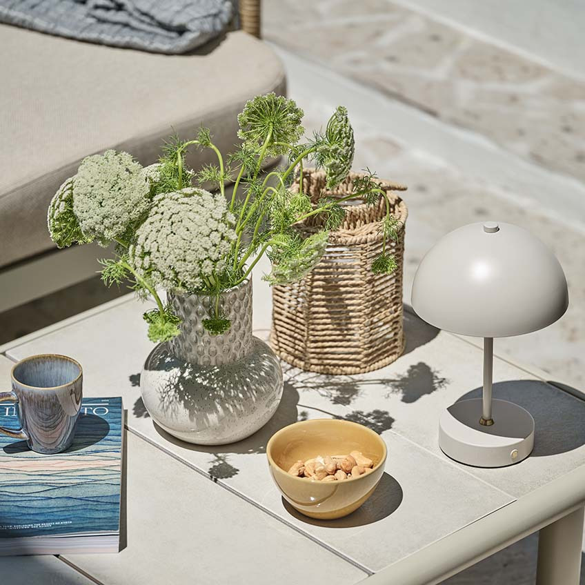 Kis kerti asztal különböző dekorelemekkel, köztük egy kis elemes lámpával, vázával és lámpással