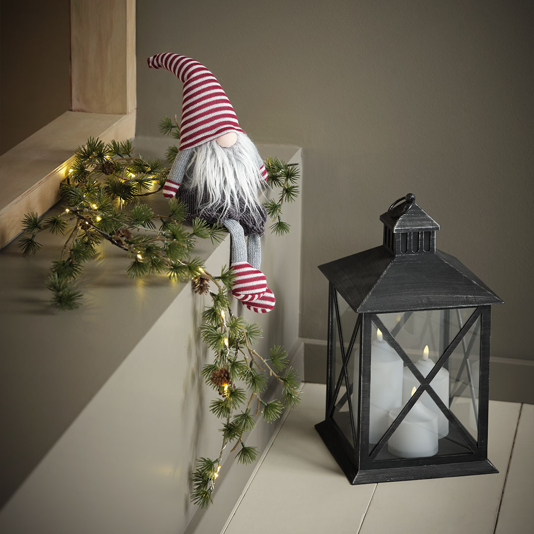 Karácsonyi manó piros csíkos sapkában, kesztyűben és zokniban, fekete lámpás mellett