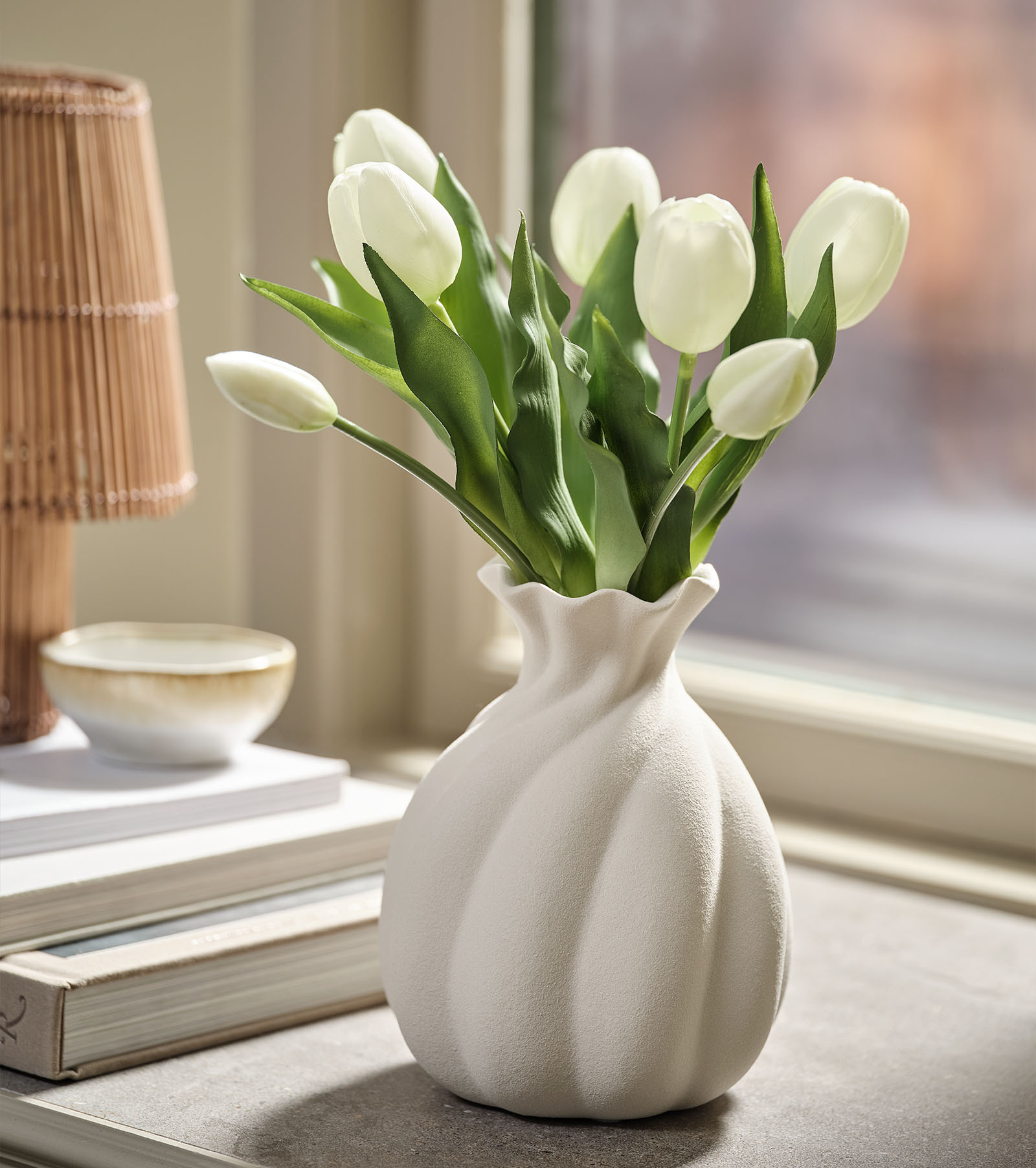 Fehér tulipánokat utánzó művirágcsokor zöld levelekkel, fehér vázában
