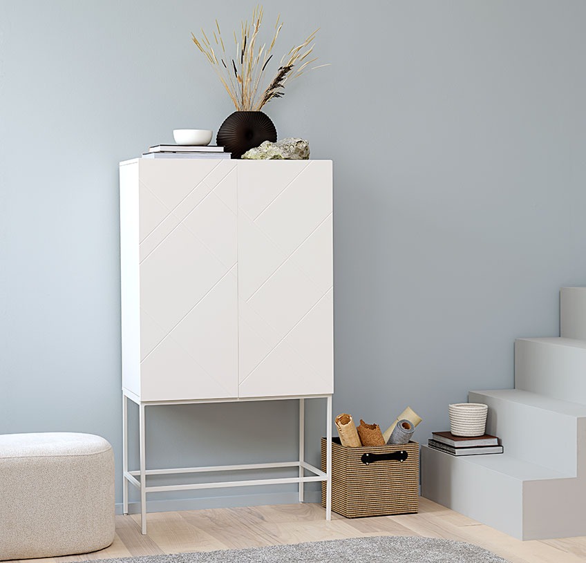 White cabinet with a black vase and other décor, a white pouffe and a storage basket in jute