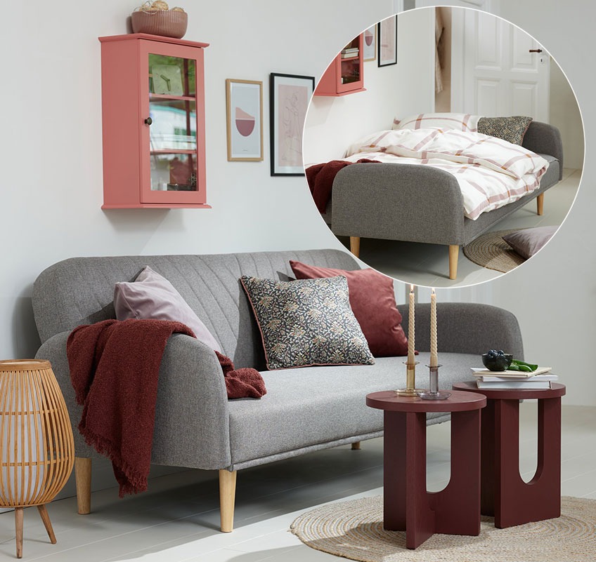 Rózsaszín fali vitrin, szürke kanapéágy és bordó kisasztalok