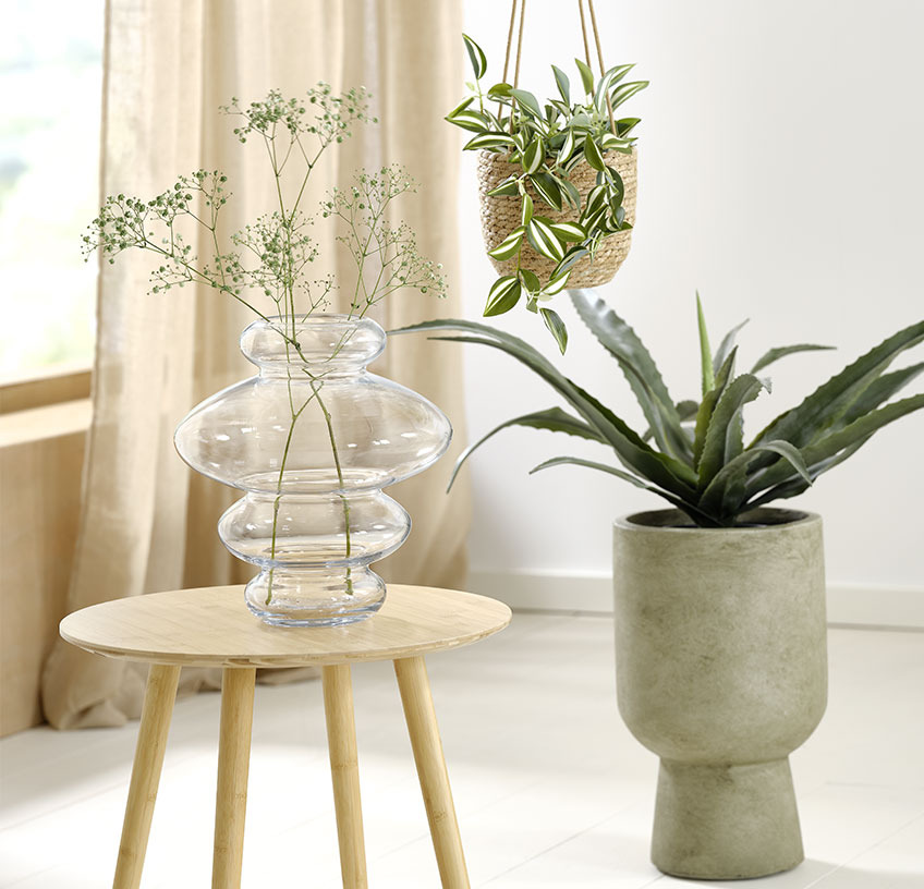 Üvegváza az asztalon, függő kaspó és zöld kaspó  mesterséges növényekkel