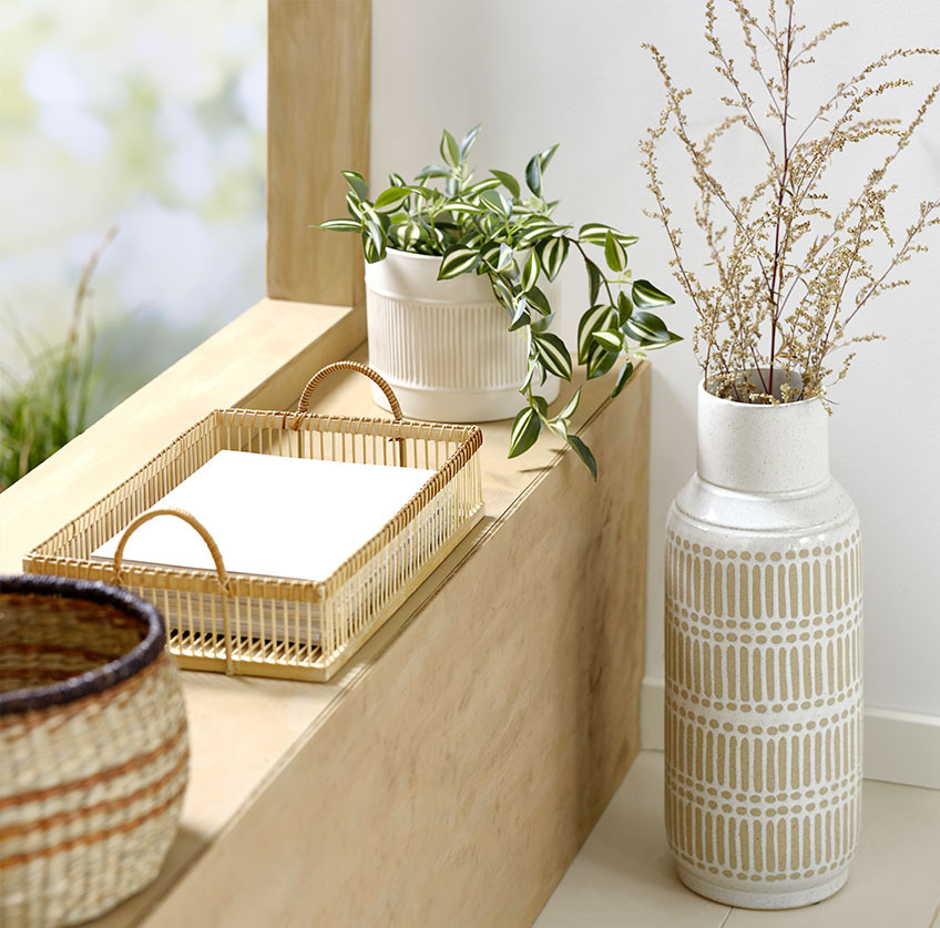 Magas váza az ablakpárkány mellett bambusz tálcával és fehér cserepes műnövénnyel