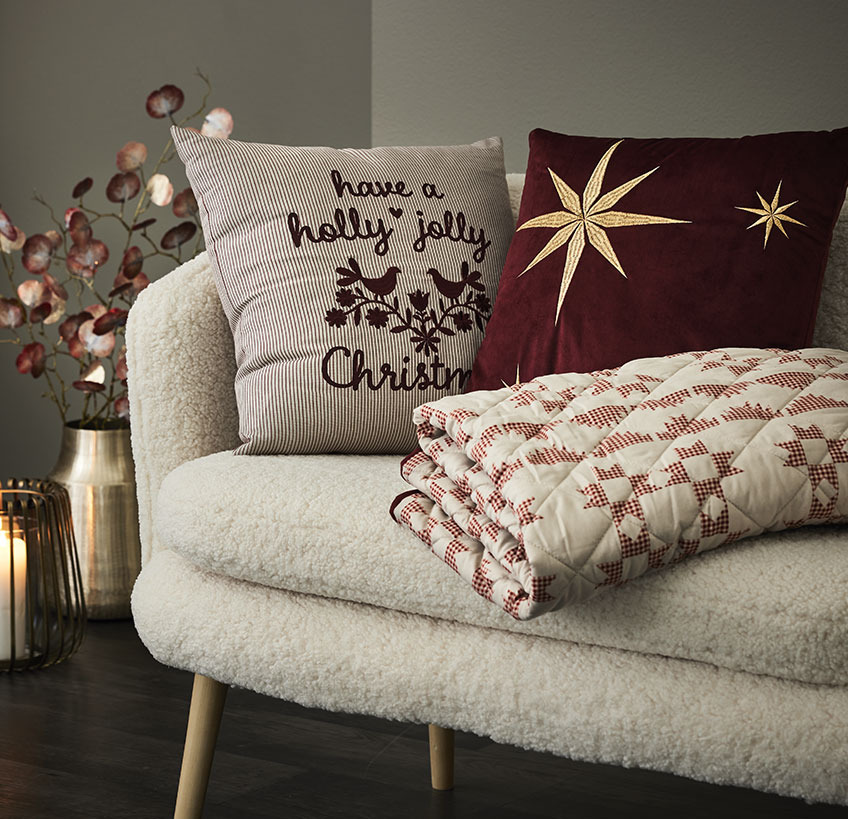 Díszpárnák és steppelt pléd karácsonyi mintákkal egy fehér kanapén
