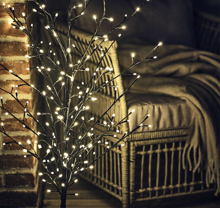 Közeli kép egy kis méretű világító fáról egy kerti szék előtt 