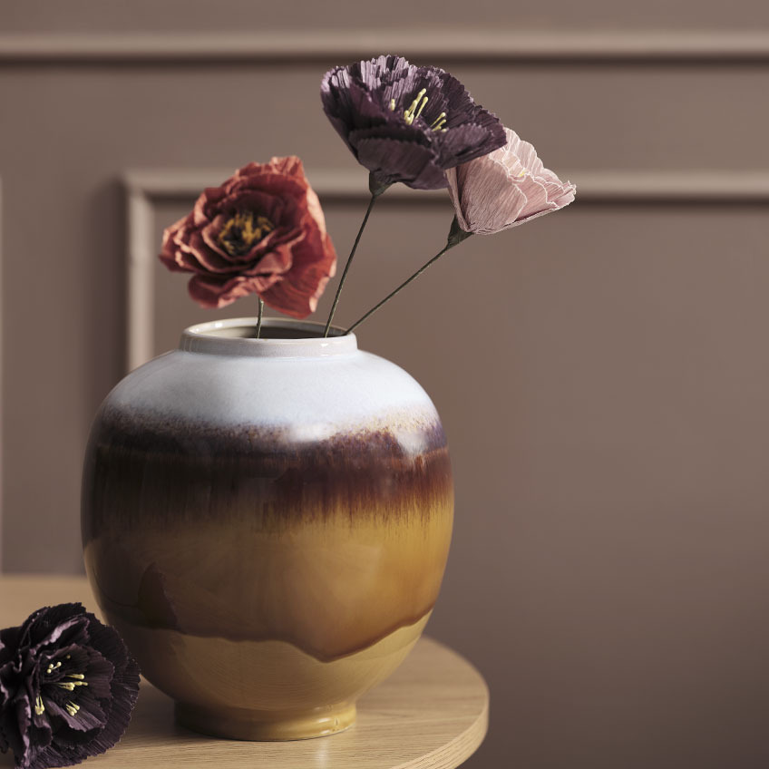 Többszínű váza egy asztalon művirágokkal piros, lila és rózsaszín színekben