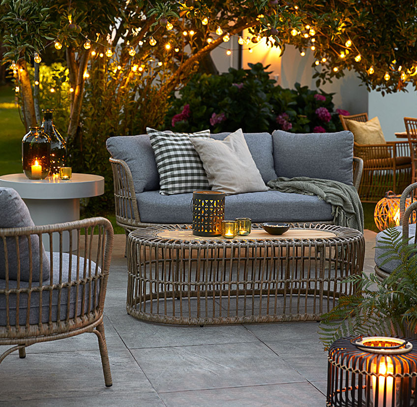Warm lighting is a great way to create the perfect summer evening atmosphere Comfortable lounge furniture on patio with string lights, battery lamps, and lanterns with candles and tealights