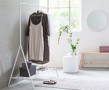 fehér ruhaállvány világos szobában ruhákkal ablak mellett