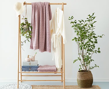 világos fa ruhaállvány szobában ruhákkal, szobanövényekkel